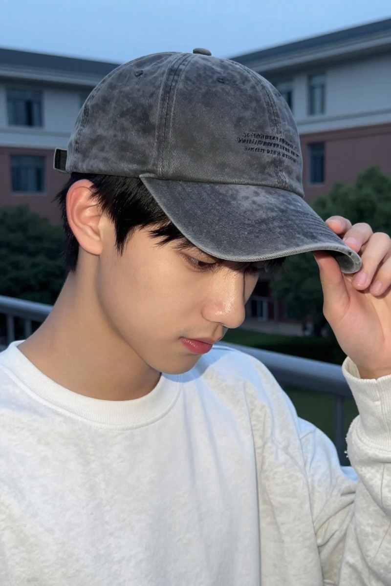 A curved-brim washed baseball cap shown close to the face in a campus-style menswear portrait